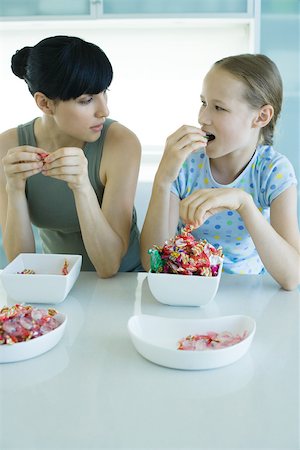 Woman and girl sitting side by side eating bowls of candy Stock Photo - Premium Royalty-Free, Code: 695-03375562