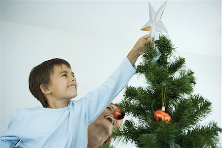 reaching for the stars - Boy and mother decorating Christmas tree, boy placing star on top of tree Stock Photo - Premium Royalty-Free, Code: 695-03376093