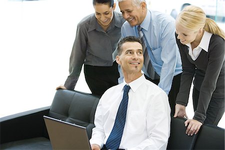 simsearch:695-03376228,k - Businessman using laptop computer, smiling, associates looking over his shoulder Stock Photo - Premium Royalty-Free, Code: 695-03376226