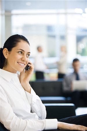 simsearch:695-03376228,k - Young businesswoman sitting in lobby, using cell phone, smiling Stock Photo - Premium Royalty-Free, Code: 695-03376242