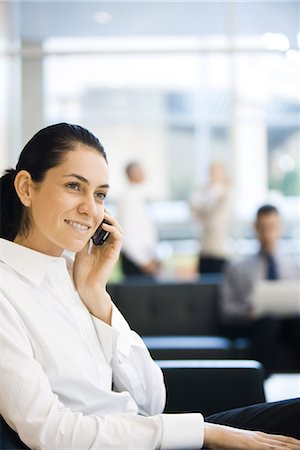simsearch:695-03376228,k - Young businesswoman sitting in lobby, using cell phone, smiling Stock Photo - Premium Royalty-Free, Code: 695-03376243