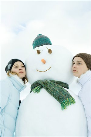 Two teenage girls leaning against snowman, looking away, portrait Stock Photo - Premium Royalty-Free, Code: 695-03376331