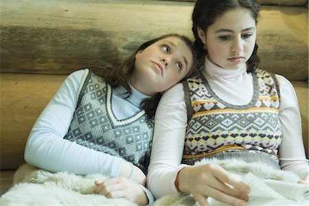 Two teen girls in winter clothes sitting under warm blanket together, one reading while other looks bored Stock Photo - Premium Royalty-Free, Code: 695-03376566