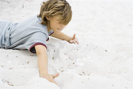 Boy lying on stomach digging in sand, close-up Stock Photo - Premium Royalty-Free, Code: 695-03377193