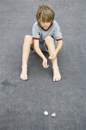 Boy sitting on the ground throwing pebbles, high angle view Stock Photo - Premium Royalty-Free, Code: 695-03377204