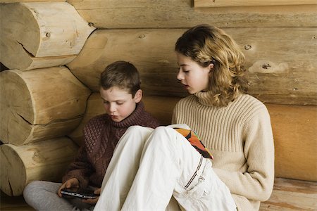 simsearch:632-03424261,k - Teen girl and preteen boy sitting side by side, reading and playing video game Stock Photo - Premium Royalty-Free, Code: 695-03377301