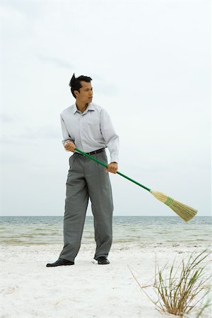 Man standing on beach sweeping with broom, looking away Stock Photo - Premium Royalty-Free, Code: 695-03377759