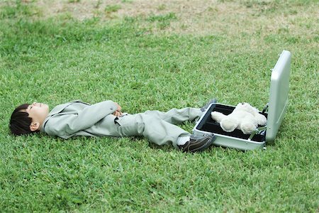 simsearch:695-05768235,k - Young boy dressed in suit, lying in grass next to open briefcase containing teddy bear Stock Photo - Premium Royalty-Free, Code: 695-03377934