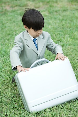 simsearch:695-05768235,k - Young boy dressed in suit, crouching in grass, opening briefcase Stock Photo - Premium Royalty-Free, Code: 695-03377933