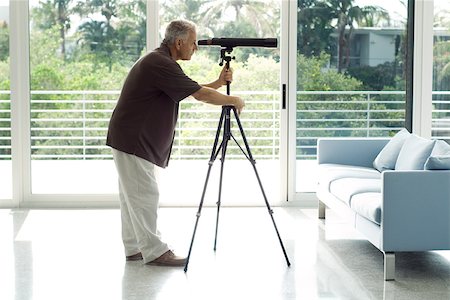 Man standing in living room, looking through telescope, side view Stock Photo - Premium Royalty-Free, Code: 695-03378277