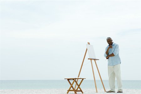 Senior man standing next to blank canvas at the beach, holding paint brushes, smiling at camera Stock Photo - Premium Royalty-Free, Code: 695-03378296