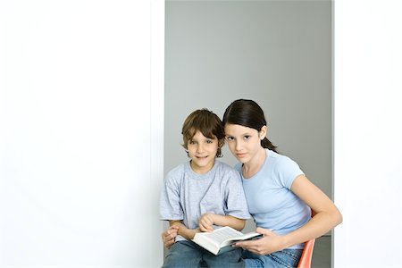 Brother and sister sitting together, girl holding book, both looking at camera Stock Photo - Premium Royalty-Free, Code: 695-03378584
