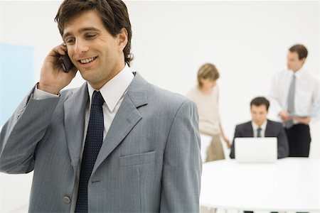 simsearch:695-03376228,k - Businessman using cell phone, smiling, colleagues in background Stock Photo - Premium Royalty-Free, Code: 695-03378695