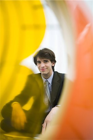 Young man in suit smiling at camera, viewed through electric fan Stock Photo - Premium Royalty-Free, Code: 695-03378932