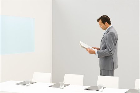 simsearch:6108-06166047,k - Businessman standing beside conference table, reading newspaper Stock Photo - Premium Royalty-Free, Code: 695-03378947