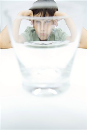 simsearch:695-03380694,k - Boy sulking at table, looking at camera through water glass Stock Photo - Premium Royalty-Free, Code: 695-03379079