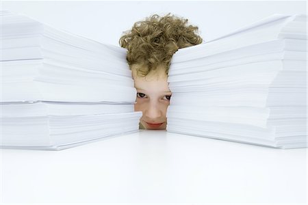 Little boy behind two large stacks of paper, peeking at camera Stock Photo - Premium Royalty-Free, Code: 695-03379071