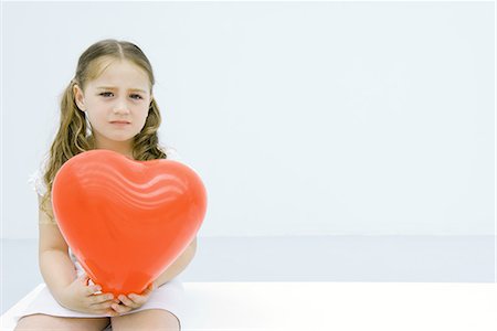 Little girl holding hear shaped balloon, looking at camera, portrait Stock Photo - Premium Royalty-Free, Code: 695-03379072