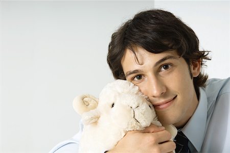 Young man holding stuffed toy against cheek, smiling at camera Stock Photo - Premium Royalty-Free, Code: 695-03379383