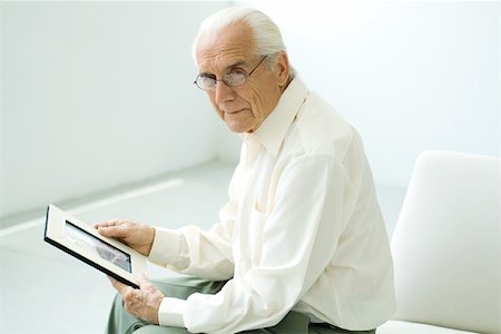 Senior man sitting, holding photograph, looking at camera Stock Photo - Premium Royalty-Free, Code: 695-03379406