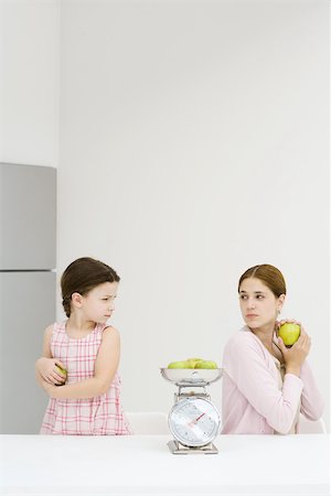 possessive - Mother and daughter weighing apples on scale, each holding apple and frowning over shoulder at one another Stock Photo - Premium Royalty-Free, Code: 695-03379423