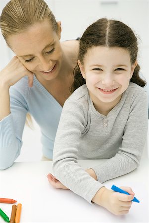 Little girl sitting on mother's lap, coloring, smiling at camera Stock Photo - Premium Royalty-Free, Code: 695-03379688