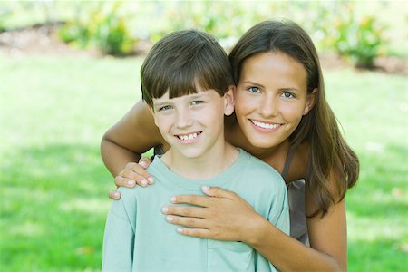 sister brother hugging two - Teen girl standing behind younger brother, hands on shoulder and heart, both smiling at camera Stock Photo - Premium Royalty-Free, Code: 695-03379889