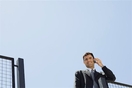 simsearch:695-03376228,k - Businessman using cell phone outdoors, smiling at camera, low angle view Stock Photo - Premium Royalty-Free, Code: 695-03379997