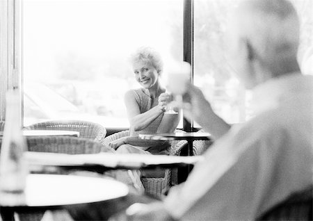 flirt senior woman - Mature man and woman looking at each other across the room in a cafe, raising glasses, blurred foreground, B&W Stock Photo - Premium Royalty-Free, Code: 695-03384135
