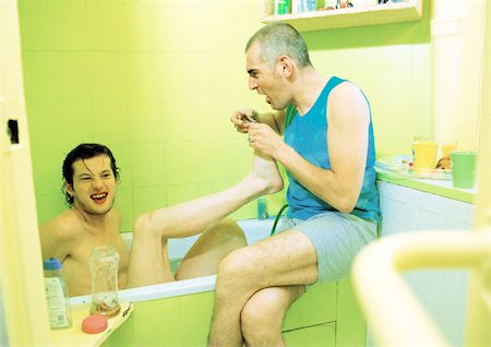 L'homme assis dans le bain, les pieds dans la main de l'homme deuxième sur bord de baignoire, vue latérale. Photographie de stock - Premium Libres de Droits, Code: 695-03385903