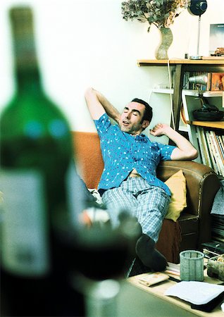 drunken - Man stretching on sofa, bottle of wine in foreground Stock Photo - Premium Royalty-Free, Code: 695-03385916
