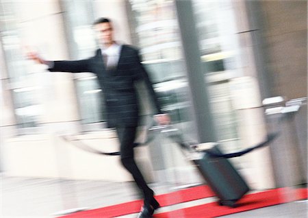 Businessman with luggage, arm extended, blurred Stock Photo - Premium Royalty-Free, Code: 695-03386888