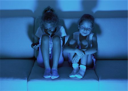 Two little girls sitting on sofa watching television in dark, laughing Stock Photo - Premium Royalty-Free, Code: 695-03387198