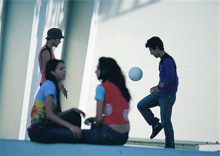 friends playing football - Two women talking in foreground, blurred, two men playing soccer Stock Photo - Premium Royalty-Free, Code: 695-03387552