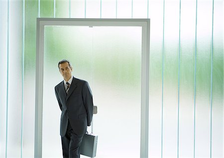 Businessman standing in front of door, holding briefcase behind back Stock Photo - Premium Royalty-Free, Code: 695-03388328