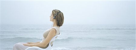 simsearch:632-03500607,k - Woman sitting in chair, listening to headphones, sea in background Stock Photo - Premium Royalty-Free, Code: 695-03388728