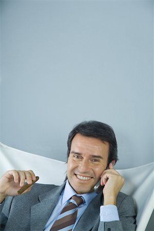 simsearch:695-03376228,k - Businessman using cell phone and holding cigar, smiling at camera Stock Photo - Premium Royalty-Free, Code: 695-03388944
