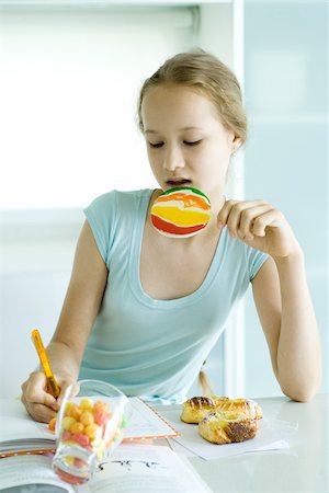 Girl doing homework and eating junk food Stock Photo - Premium Royalty-Free, Code: 695-03389119