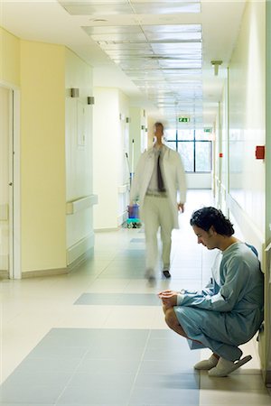 simsearch:632-01613036,k - Male patient crouching in hospital corridor, looking down, doctor walking in background Stock Photo - Premium Royalty-Free, Code: 695-03389308