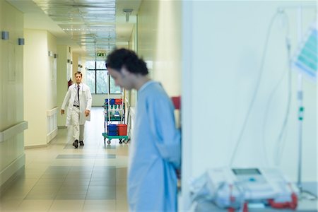 simsearch:632-01613036,k - Male doctor walking in hospital corridor, patient in foreground Stock Photo - Premium Royalty-Free, Code: 695-03389311