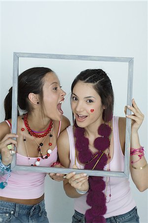 simsearch:695-03376693,k - Deux jeunes amis femmes brandissant photo frame, une crier à l'oreille de l'autre, portrait Photographie de stock - Premium Libres de Droits, Code: 695-03389421