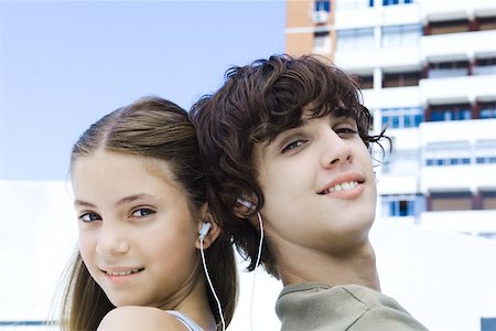 Brother and sister back to back, listening to earphones, smiling at camera Stock Photo - Premium Royalty-Free, Code: 695-03389804