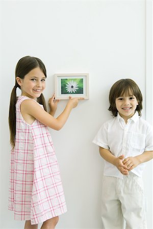 simsearch:696-03395895,k - Girl standing beside younger brother, hanging framed picture, both smiling at camera Stock Photo - Premium Royalty-Free, Code: 695-03389970