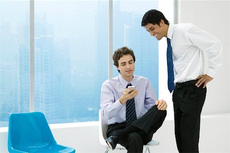Young professional showing colleague his cell phone, both smiling Stock Photo - Premium Royalty-Free, Code: 695-03380003