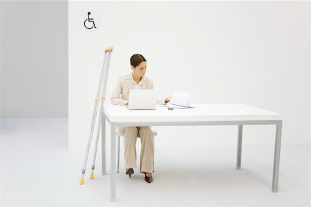 symbol for female - Professional woman working in office, crutches leaning against desk beside her Stock Photo - Premium Royalty-Free, Code: 695-03380188
