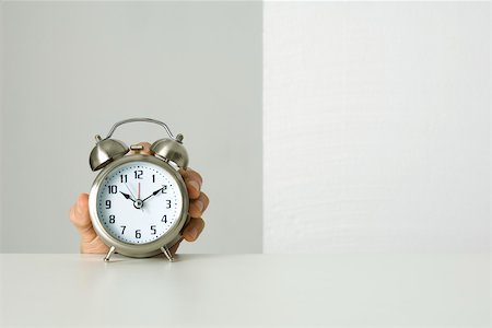 Old-fashioned alarm clock, hand reaching up to grab it from behind Stock Photo - Premium Royalty-Free, Code: 695-03380281