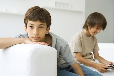 simsearch:632-03424261,k - Boys sitting on couch, one looking at camera, the other playing handheld video game Stock Photo - Premium Royalty-Free, Code: 695-03380338