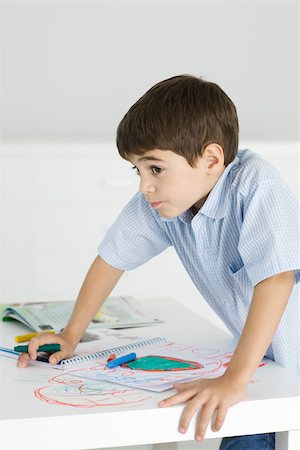 Boy leaning on table, holding crayon, colorful drawing on paper and the table Stock Photo - Premium Royalty-Free, Code: 695-03380358