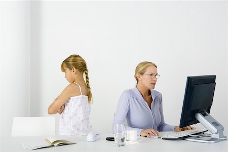 simsearch:695-03380694,k - Woman sitting at table using desktop, daughter standing nearby with her back turned and arms folded Stock Photo - Premium Royalty-Free, Code: 695-03380368