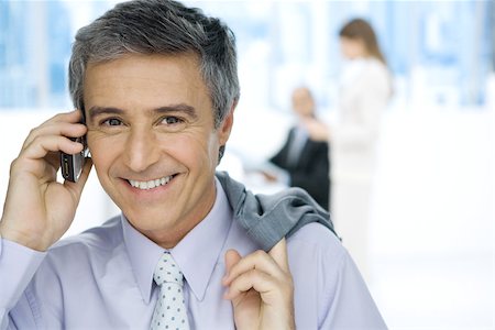 simsearch:695-03376228,k - Businessman using cell phone, smiling at camera, jacket slung over shoulder Stock Photo - Premium Royalty-Free, Code: 695-03380519